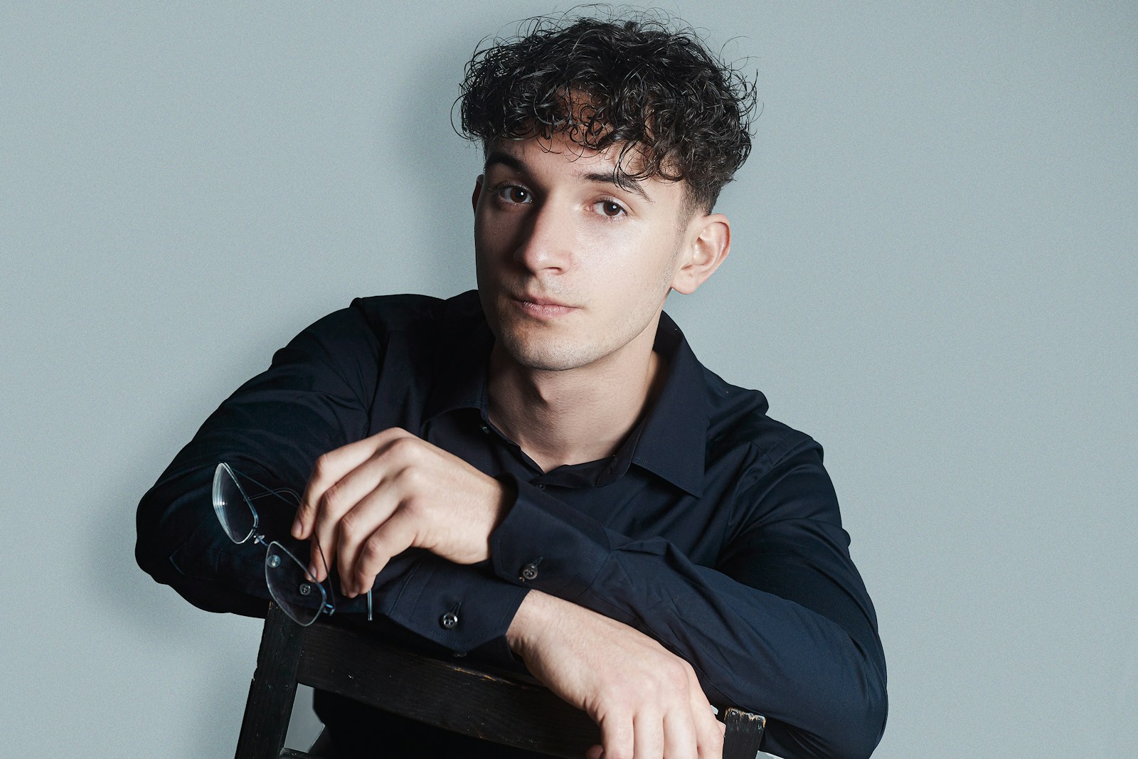 un jeune bloggeur passionné assis sur une chaise tenant une paire de lunettes